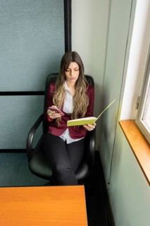 Young blonde business woman sitting in her office using the phone while checking notes