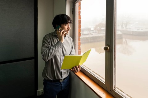 Latino businessman working in an office overlooking the river. Talking on the phone and reviewing notes while he looks out the window