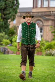 Man in Bavarian traditional costume with hat walking across lawn