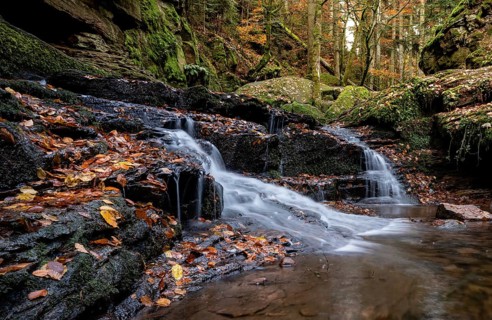 Landscape photograph of a small waterfall with stones and leaves in autumn