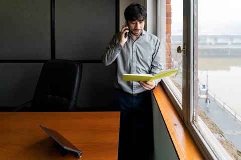 Latino businessman working in an office overlooking the river. Talking on the phone and reviewing notes