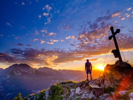 Mountaineer standing at sunset at the summit cross of the Brettgabel