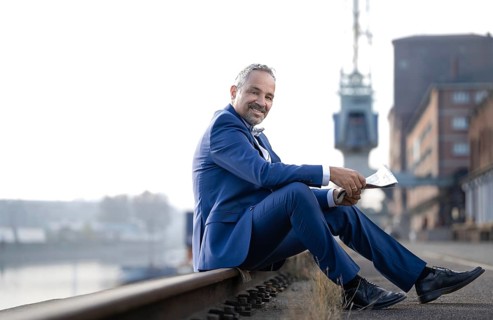 Man in blue suit sitting on railway track reading newspaper