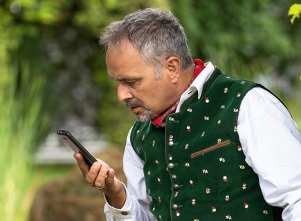 Middle-aged man in Bavarian traditional costume looking confused at his phone