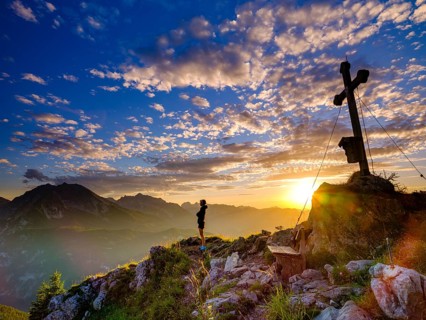 Mountaineer standing at sunset at the summit cross of the Brettgabel