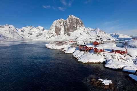Rorbuer huts and wooden racks with stockfish to dry by Hamnoy fjord in the snow in winter
