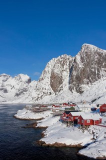 Rorbuer huts and wooden racks with stockfish to dry by Hamnoy fjord in the snow in winter