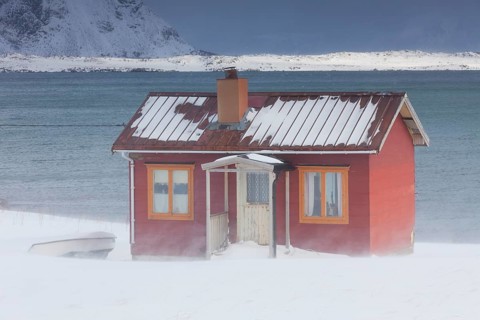 Red insulated wooden hut along the coast in the snow in winter