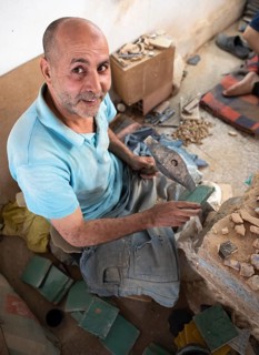 Moroccan cellular craftsman at work: hammering small pieces out of a tile