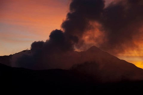 Smoke rising from volcano at sunset
