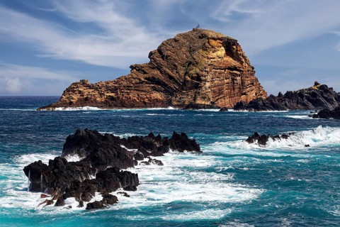 Rocks unswept by surf at the back small rocky island Ilheu Mole with lighthouse Farol do Porto Moniz