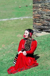 Georgian woman from a folkloric group sitting on the ground in front of a tower