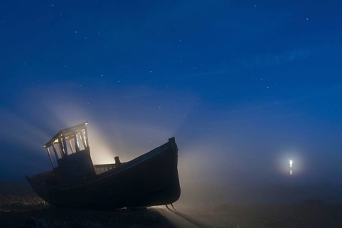 Abandoned fishing boat on a shingle beach at night