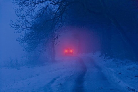 Distant brake lights of a car on a snow-covered road in freezing fog at dusk