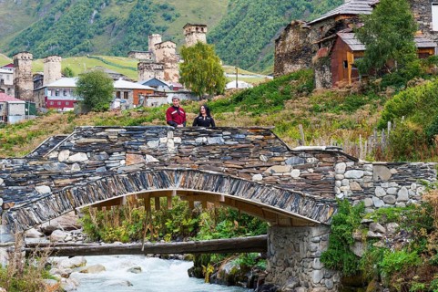 Georgian couple from a folklore group on a stone bridge outside the village of Ushguli