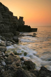 View of waves on rocky beach and old quarry on cliffs at sunset