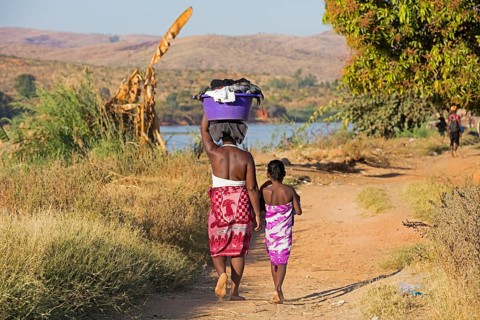 Malagasy daughter and mother carrying a laundry basket on their heads while walking along the Tsiribihina River