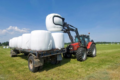 Plastic wrapped round silage bales stacked on trailer with mechanical loader