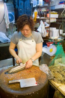 Woman preparing fish next to frogs in a net at the fish market
