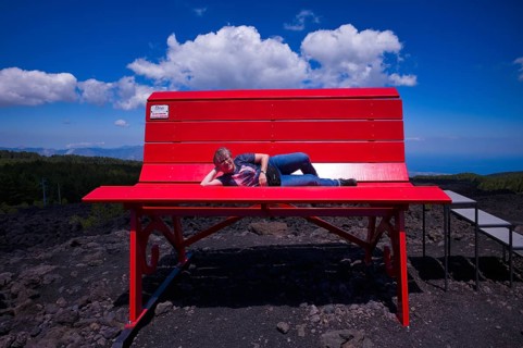 Elderly woman lying on huge red bench