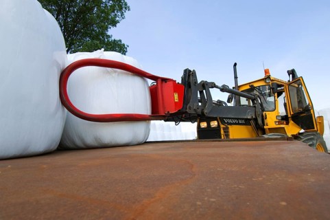 Plastic wrapped round silage bales stacked on trailer with mechanical loader