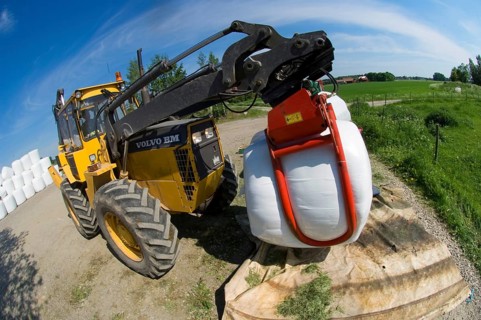 Plastic wrapped round silage bales stacked on a pile with mechanical loader