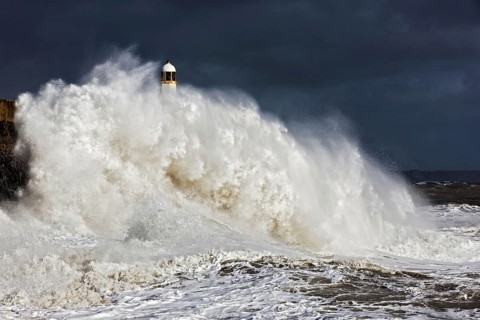 Coastal town seafront and lighthouse bombarded by waves in storm
