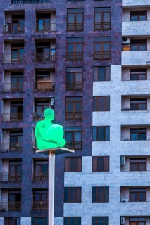 Illuminated human sculpture on a pole in front of a building seen from the Yerevan Cascade