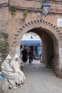 Men with djellaba sitting next to the medina arch in the city