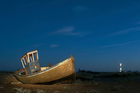 Abandoned fishing boat on shingle beach illuminated by torchlight at night