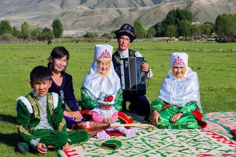 Kazakh family in traditional dress listening to the music of an accordion player
