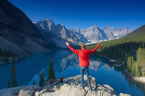 Tourist with open arms at the viewpoint overlooking Moraine Lake in the Valley of the Ten Peaks