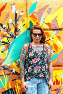 Tattooed woman in front of a wall covered with graffiti