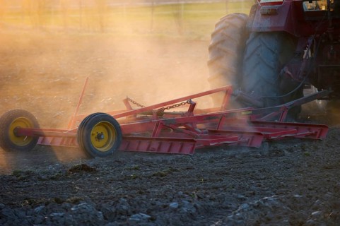 Close-up of Vaderstad cultivator cultivating a field planting bed in a dusty field at sunset