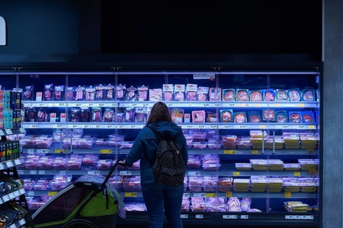 A woman with a pram is standing in front of the meat and sausage cooling shelf