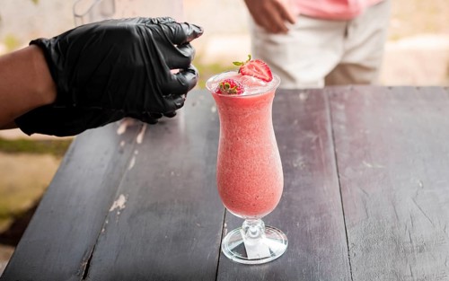Hands decorating a strawberry smoothie on wooden table. Close up of hands making strawberry smoothie on wooden table. Close up of person decorating strawberry milkshake on table