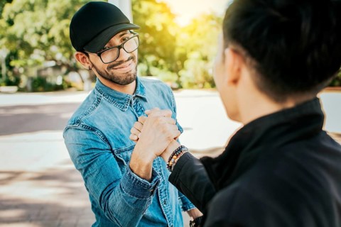 Concept of two friends greeting each other and shaking hands on the street. Two teenage friends shaking hands at each other outdoors. Two people shaking hands on the street