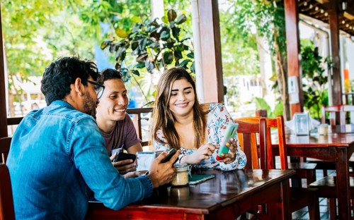 Young friends in a coffee shop with their cell phones having a good time. Three people in a coffee shop with phones having a good time. Three teenage friends on their cell phones in a coffee shop