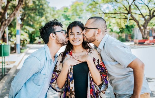 Two men kissing a girl cheek. Portrait of two guys kissing a girl cheek. Two young men kissing a woman cheek outdoor