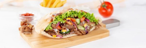 Doener Kebab Doner Kebap half fast food meal in pita bread with fries on wooden board Panorama in Stuttgart