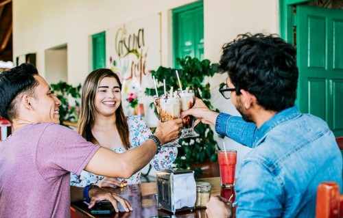 Happy friends enjoying a milkshake in a coffee shop. Three happy best friends meeting and toasting in a coffee shop