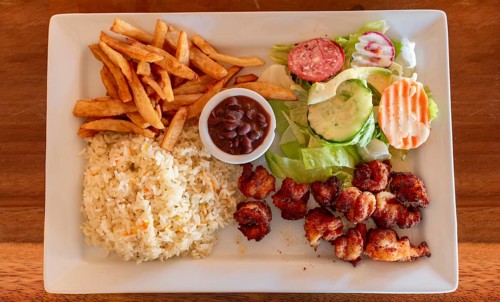 Plate of breaded shrimp with rice and salad on the wooden table. Top view of breaded shrimp with french fries and salad served on wooden table. Seafood food concept served on the table