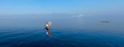 Panorama of traditional Burmese fisherman balancing with fishing net at Inle lake