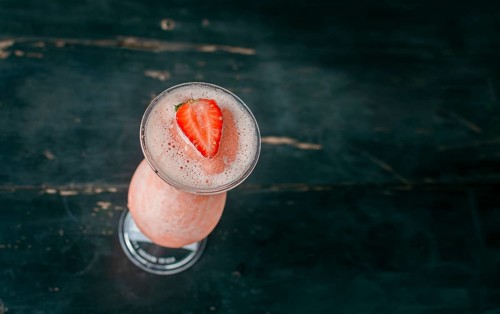 View of strawberry milkshake on dark wood. View from above of delicious strawberry smoothie with a strawberry on top on wood. Top view of strawberry smoothie on dark wooden table