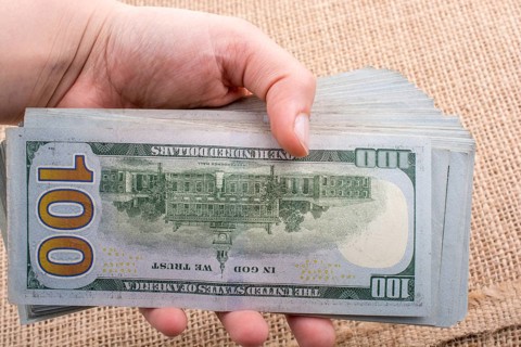 Hand holding banknote bundle of US dollar on a linen canvas background