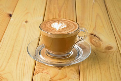 Cappuccino in transparent glass cup on wooden table