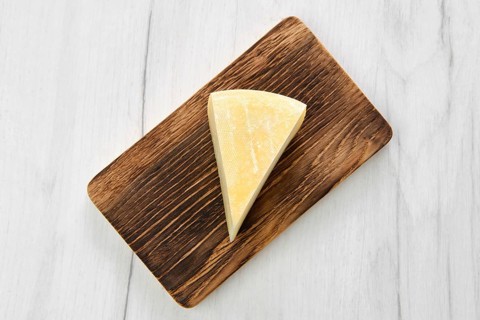 Top view of triangular piece of goat cheese on wooden cutting board