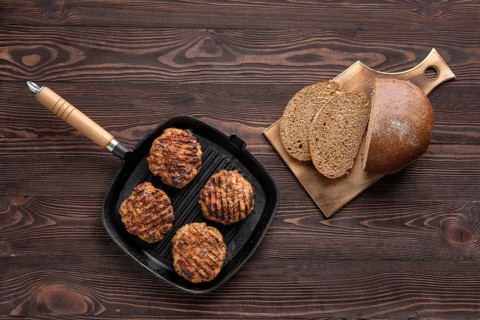 Top view of cast iron grill pan with beef cutlets and freshly baked brown bread