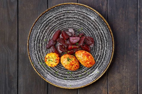 Top view of plate with fried pork cutlet with roasted beetroot slices and grilled maize on dark wooden table