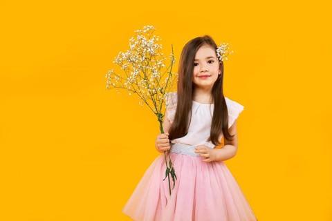 Cute young girl with wildflowers bouquet in hands on yellow background